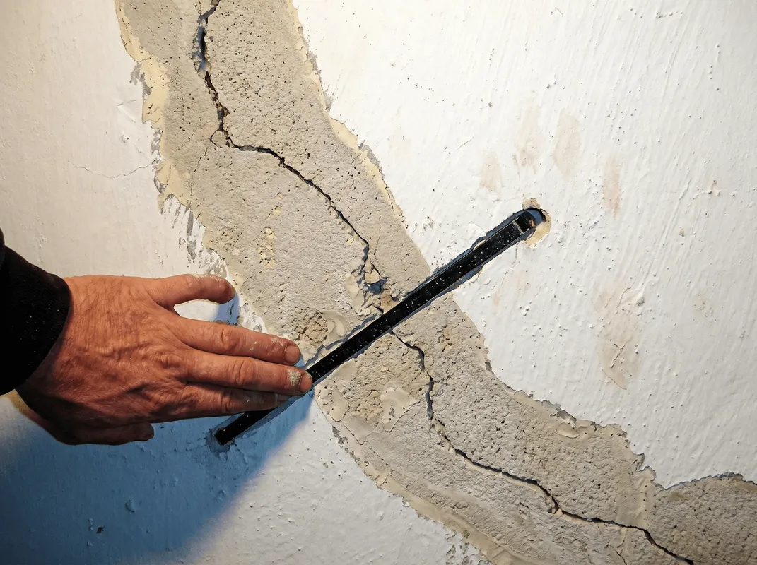 A wall with a large crack is being inspected by a professional in Staten Island, NY